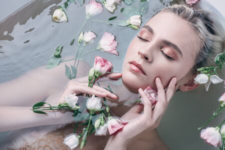 top view of beautiful woman lying in water with closed eyes among flowers in white bathtubの写真素材