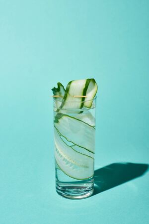 Transparent glass with fresh water and cucumber slices on turquoise backgroundの写真素材