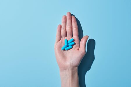 Cropped view of woman holding blue pills on palm on blue backgroundの写真素材