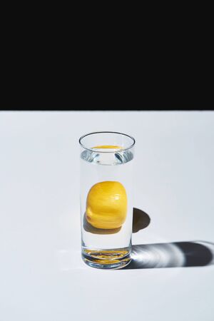 Transparent glass with water and whole lemon on white surface isolated on black backgroundの写真素材