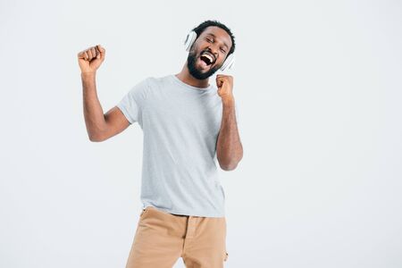 Excited African American man singing and listening music with headphones, isolated on grey backgroundの写真素材
