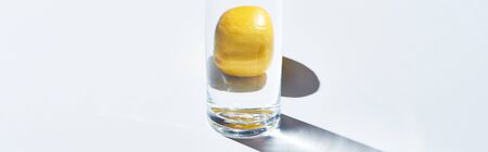 Panoramic shot of transparent glass with water and whole lemon on white backgroundの写真素材