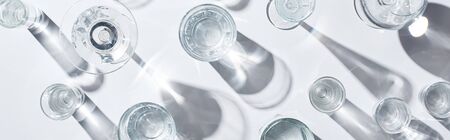Top view of transparent glasses with clear water on white background with shadows, panoramic shotの写真素材