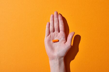 Partial view of woman holding orange pill on orange backgroundの写真素材