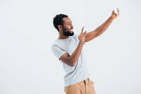 African American man with victory sign taking selfie on smartphone, isolated on grey backgroundの写真素材