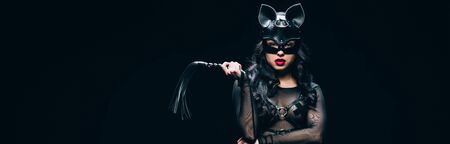 Panoramic shot of sexy young brunette woman in bdsm costume and mask with leather flogging whip...