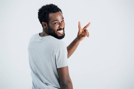 Happy African American man in grey t-shirt showing victory sign isolated on grey backgroundの写真素材