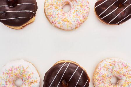 Top view of chocolate glazed and white doughnuts with sprinkles on white background