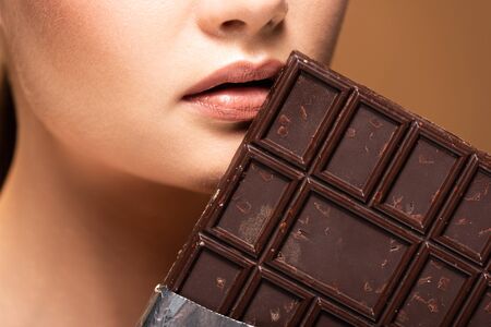 Partial view of beautiful young woman holding chocolate bar isolated on beige backgroundの写真素材