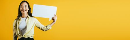Happy Asian girl holding speech bubble, isolated on yellow backgroundの写真素材