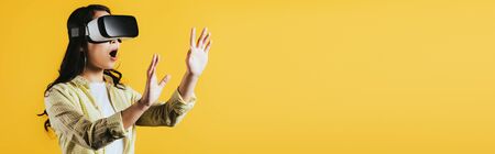 Surprised woman gesturing and using Virtual reality headset, isolated on yellow backgroundの写真素材