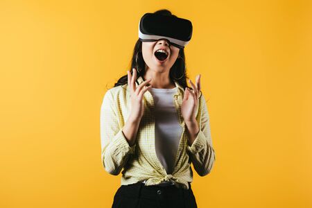 Excited girl yelling in Virtual reality headset, isolated on yellow background