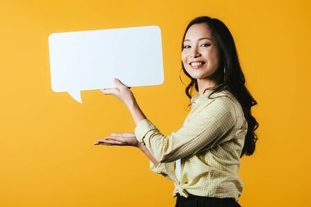 Beautiful smiling Asian girl presenting speech bubble, isolated on yellow backgroundの写真素材