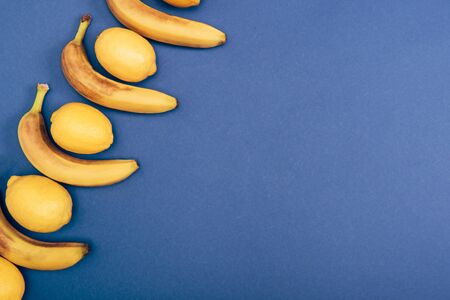 Top view of yellow lemons and bananas on blue background with copy spaceの写真素材