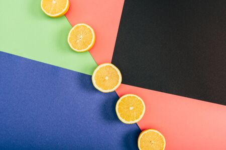 Top view of fresh and yellow cut lemons on multicolored black blue green coral backgroundの写真素材