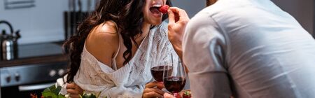 Cropped view of man feeding woman with strawberry, panoramic shot