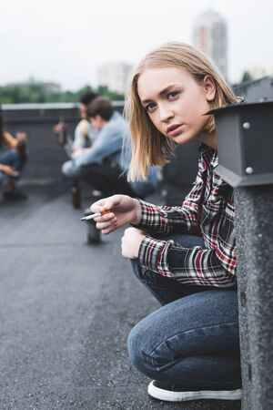 Selective focus of blonde and pretty teenager smoking cigarette and looking awayの写真素材