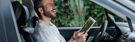 Panoramic shot of happy man holding digital tablet in car