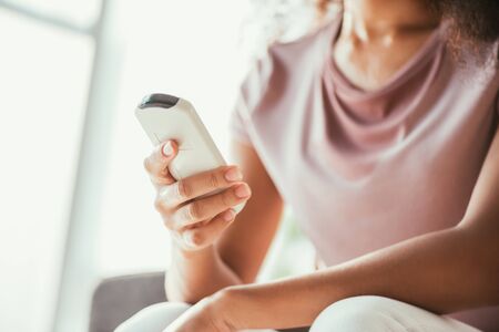 Cropped view of African american woman holding air conditioner remote controller while suffering...