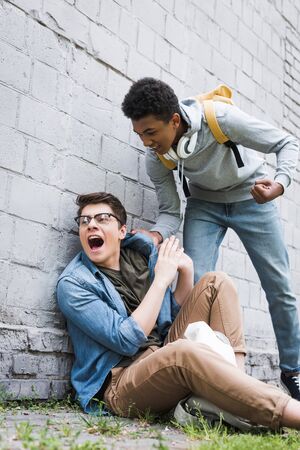 Aggressive and brunette African american boy going to punch frightened boy in glassesの写真素材