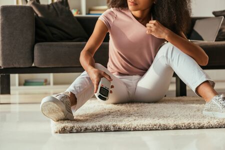 Cropped view of African american woman sitting on floor and holding air conditioner remote controllerの写真素材