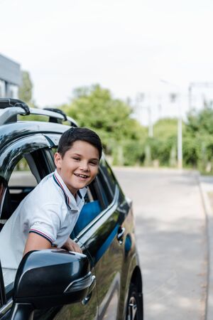 Positive boy smiling and looking at camera from car windowの写真素材