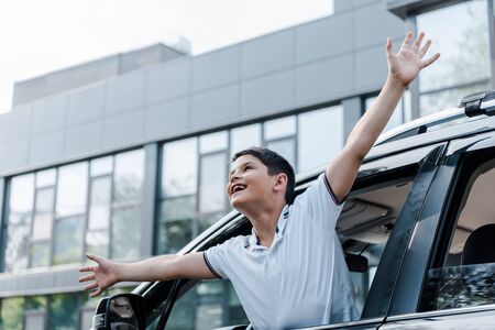 Low angle view of happy kid with outstretched hands in car window