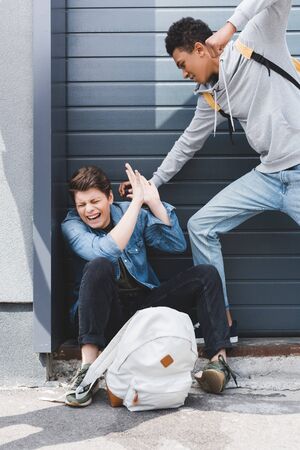 African american boy in hoodie and jeans punching scared boyの写真素材