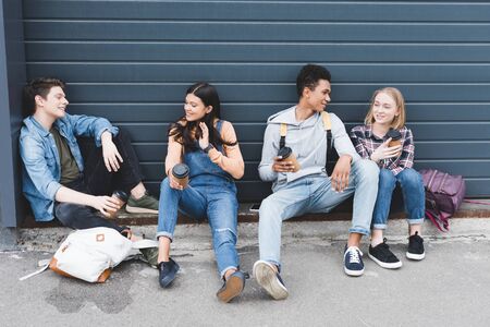 Teenagers sitting, drinking coffee from disposable cups and talking