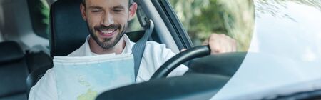 Panoramic shot of happy driver sitting in car and looking at mapの写真素材