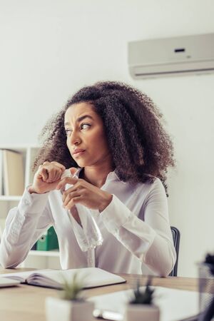 Selective focus of dissatisfied African american businesswoman looking away while holding plastic...