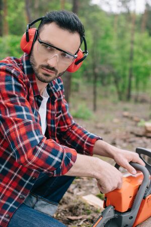 Serious lumberjack in earmuffs and hearing protectors looking away in forestの写真素材