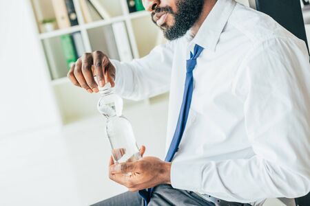 Partial view of African american businessman opening plastic bottle with water while suffering from heatの写真素材