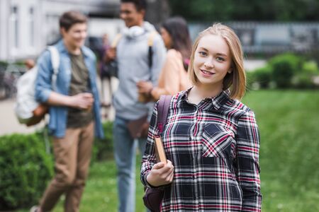 Smiling blonde teenager holding book and looking at camera