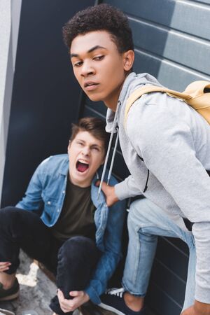 Selective focus of African american boy in hoodie and jeans bulling screaming and scared boyの写真素材