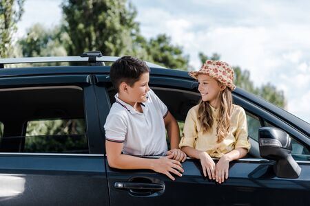 Happy kid in straw hat looking at brother from car windowの写真素材