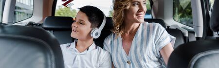 Panoramic shot of cheerful kid in headphones near mother in carの写真素材
