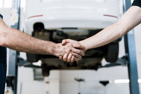 Cropped view of car mechanic shaking hands with man in garageの写真素材