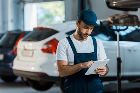 Bearded car mechanic in cap using digital tablet near carsの写真素材
