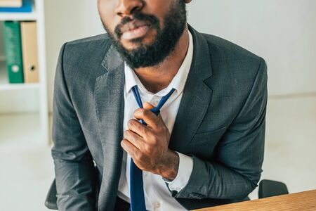 Partial view of African american businessman touching tie while suffering from heat in officeの写真素材