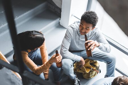 High angle view of teenagers talking, sitting on stairs and holding beerの写真素材