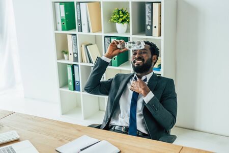 African american businessman holding plastic bottle with water near head while suffering from summer heat in officeの写真素材