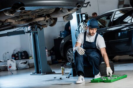 Handsome bearded man in cap looking at toolbox near carsの写真素材
