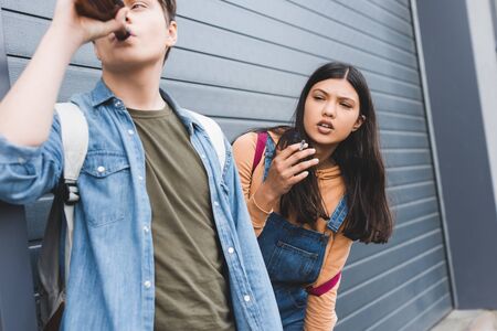 Boy and brunette teenager looking away, smoking cigarette and drinking beerの写真素材