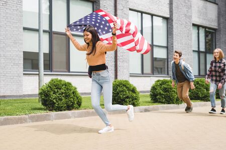 Happy teenagers smiling, holding american flag and running outsideの写真素材