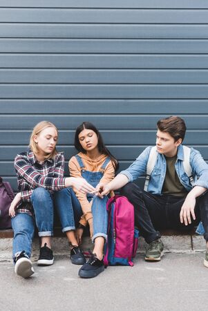Brunette and blonde teenagers sitting, smoking cigarette and speaking