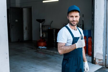 Handsome bearded car mechanic in cap standing and showing thumb upの写真素材