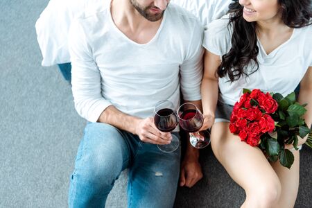 Overhead view of smiling couple clinking with glasses of red wine and woman holding bouquet of red rosesの写真素材