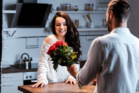 Man gifting bouquet of roses to smiling woman at kitchenの写真素材