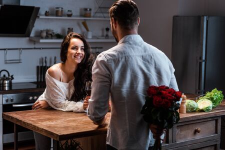 Man holding bouquet of roses behind back and looking at smiling womanの写真素材